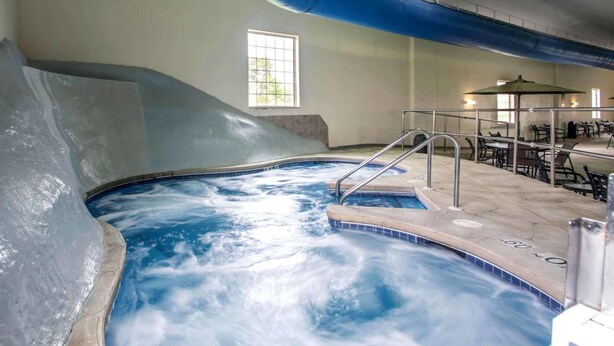 Un bain à remous agrémenté d’une cascade, un espace détente avec des tables et des chaises, et une fenêtre laissant entrer la lumière naturelle.