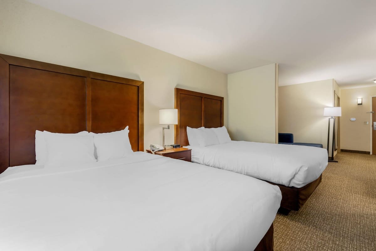 A hotel room with two beds, wooden headboards, bedside lamps, a nightstand, and a carpeted floor.