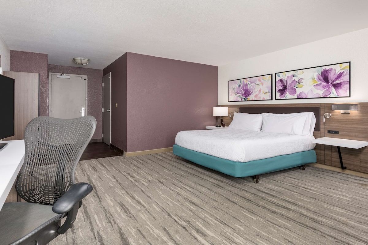 Habitación de hotel con cama, escritorio, silla y dos cuadros florales en la pared.