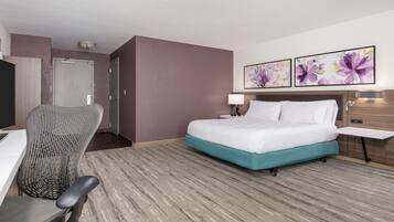 A hotel room with a bed, a desk, a chair, and two floral paintings on the wall.