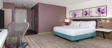 Une chambre d’hôtel avec un lit, un bureau, une chaise et deux tableaux représentant des motifs floraux accrochés au mur.