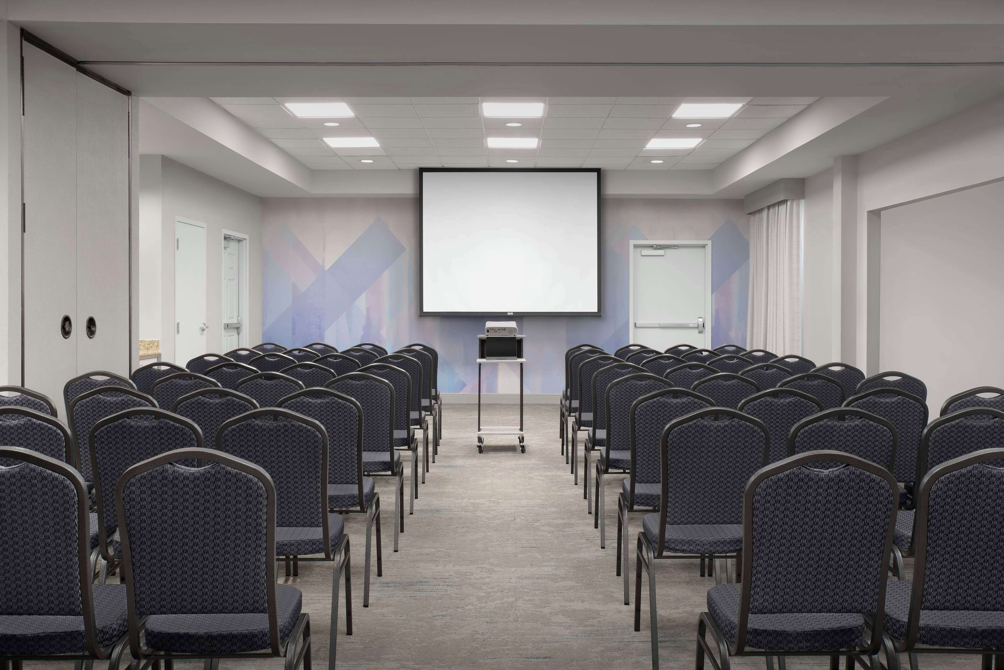 A conference room with rows of chairs, a projector screen, and a presentation podium.