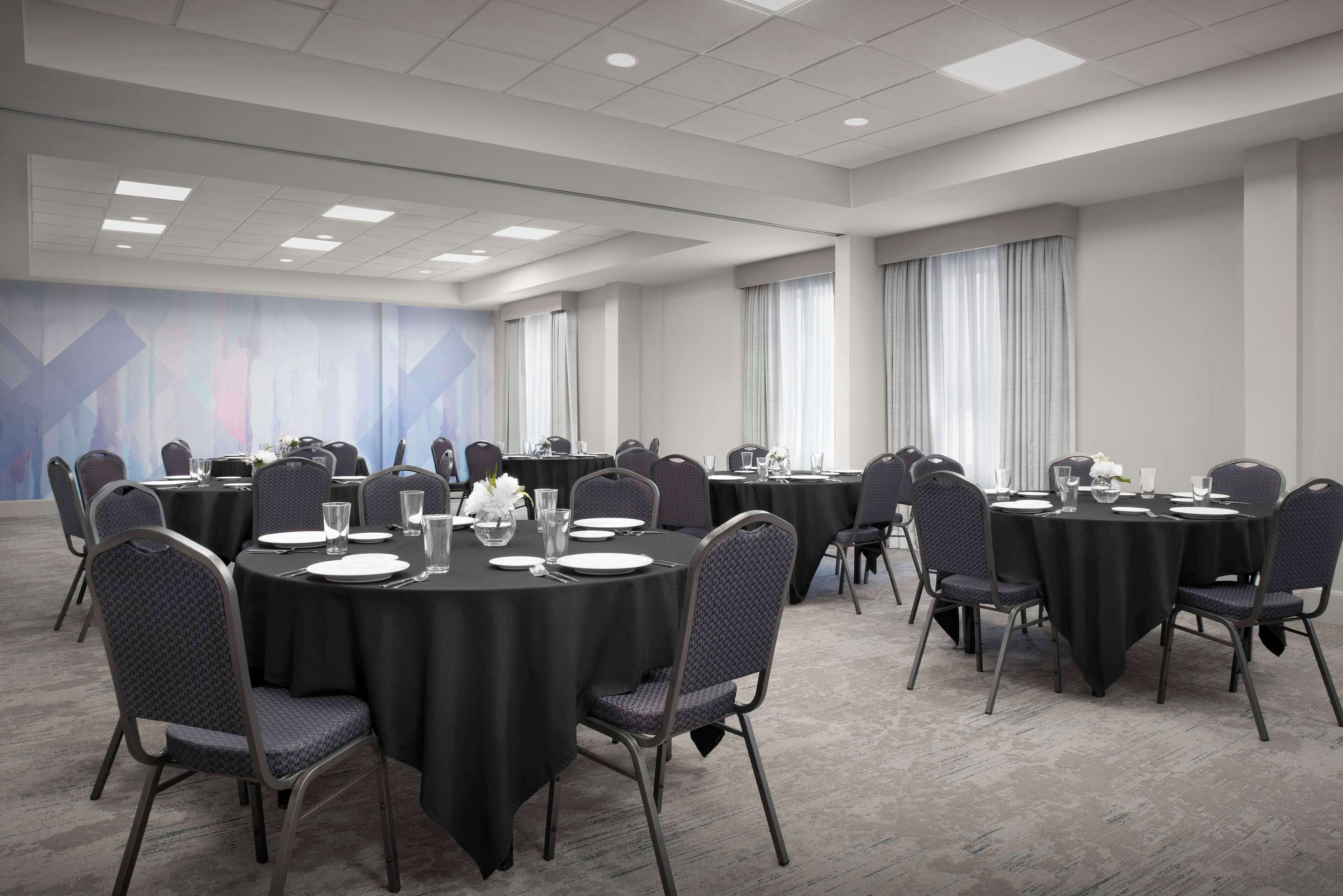 A conference room with multiple round tables, each set with chairs, plates, glasses, and cutlery.
