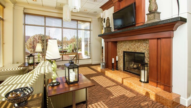 A spacious living room with a fireplace, large windows, and a flat-screen TV mounted above the mantel. - Hilton Garden Inn Anderson (Anderson)