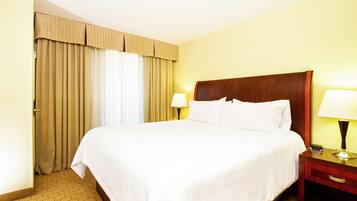 A hotel room with a large bed, two bedside tables, a wooden headboard, and beige curtains.