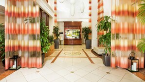 A hotel lobby with a reception desk, potted plants, and a tiled floor. - Hilton Garden Inn Anderson (Anderson)