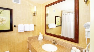A bathroom with a granite countertop sink, a large mirror, and a hairdryer on the wall.