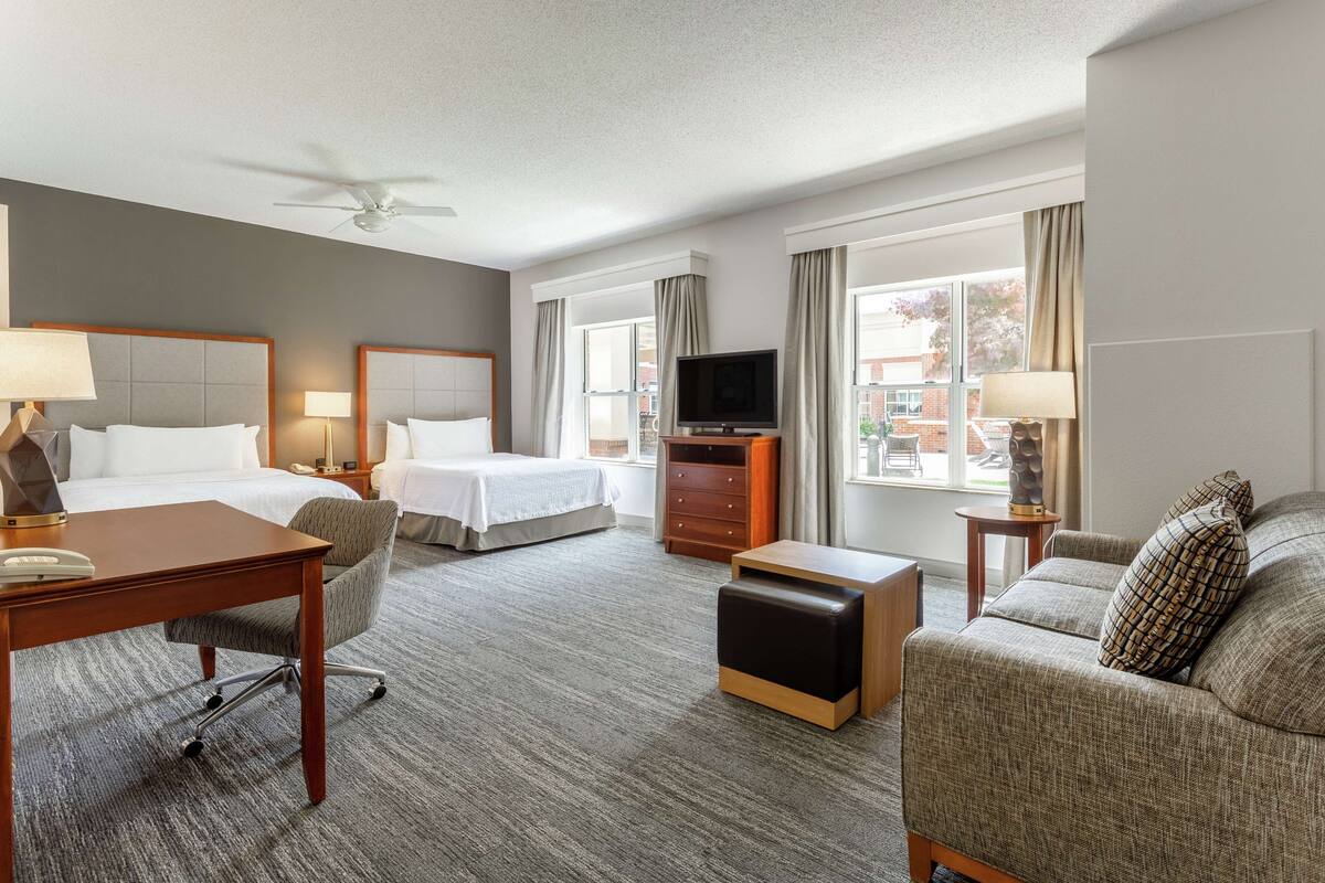 A hotel room with a bed, a desk, a chair, a sofa, a television, and a window with curtains.