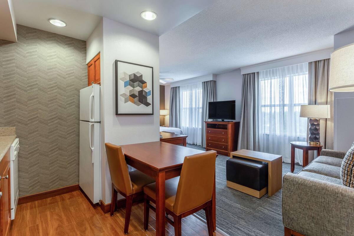 A hotel room with a dining area, a sofa, a TV, and a lamp.