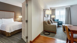 A hotel room with a bed, a sofa, a dining table, and a lamp. - Homewood Suites by Hilton Albany (Albany)