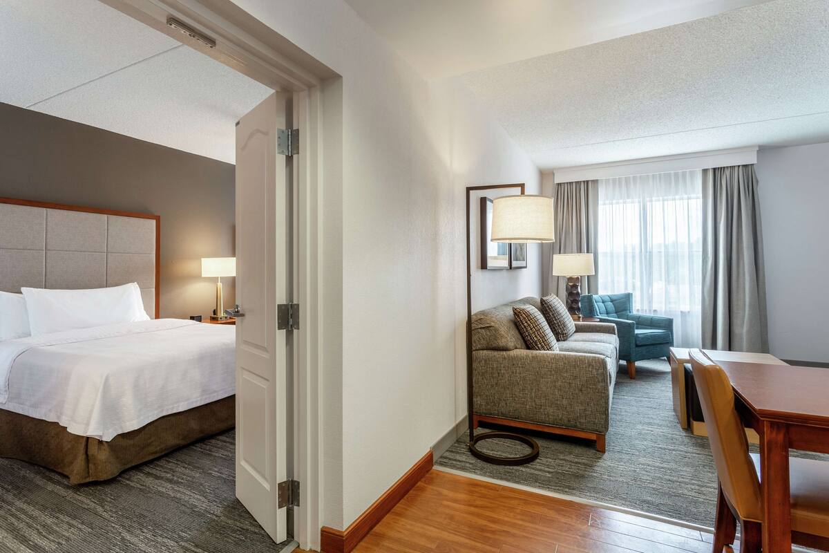 A hotel room with a bed, a sofa, a dining table, and a lamp.