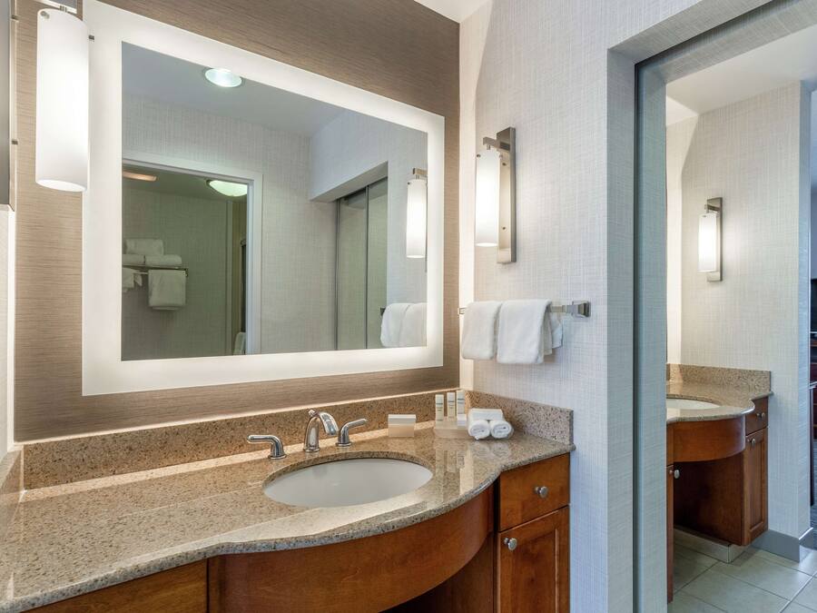 A modern bathroom with a large mirror, granite countertop, and wooden cabinets.