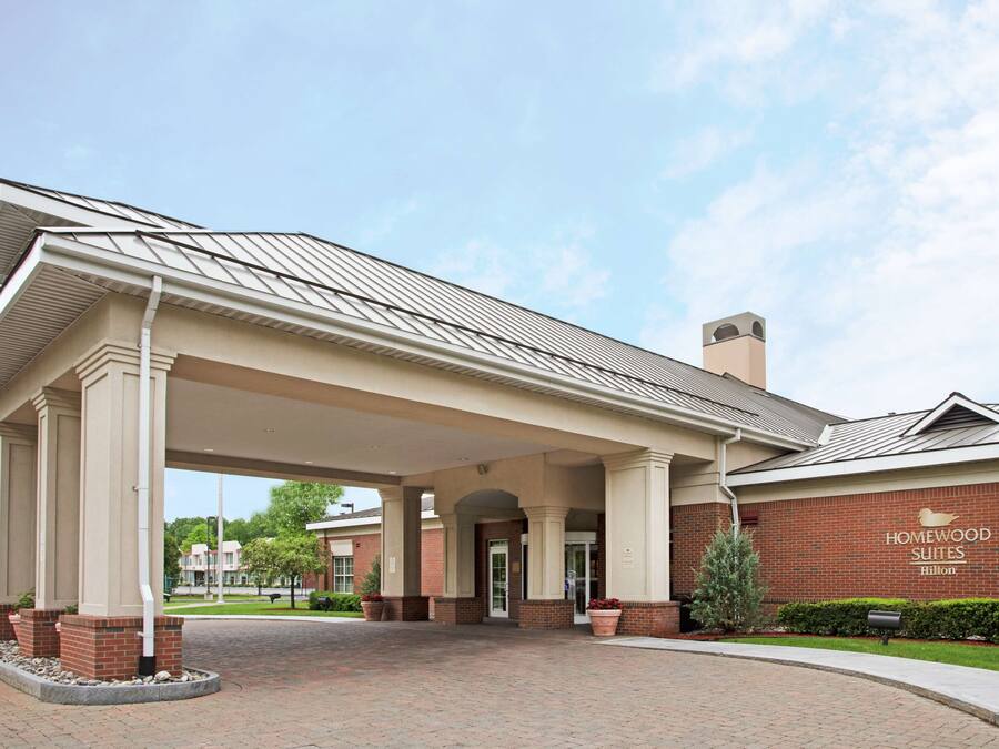 Entrada de un hotel con un paseo techado, fachada de ladrillo y un letrero de Homewood Suites Hilton.