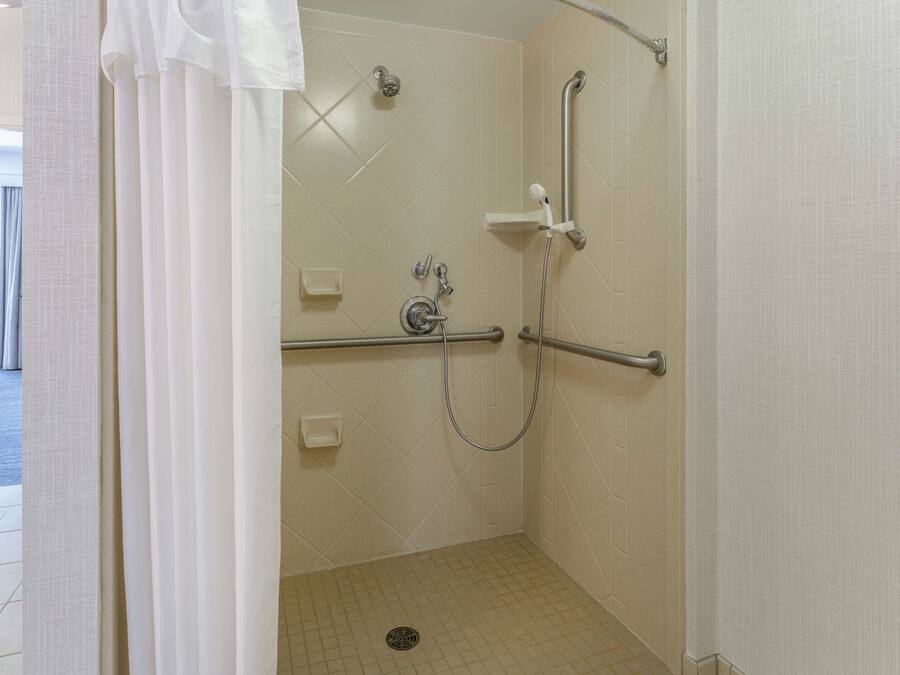 A walk-in shower with a handrail, a handheld showerhead, and a floor drain.