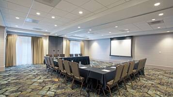 A conference room with a long table, chairs, a projector screen, and a carpeted floor.
