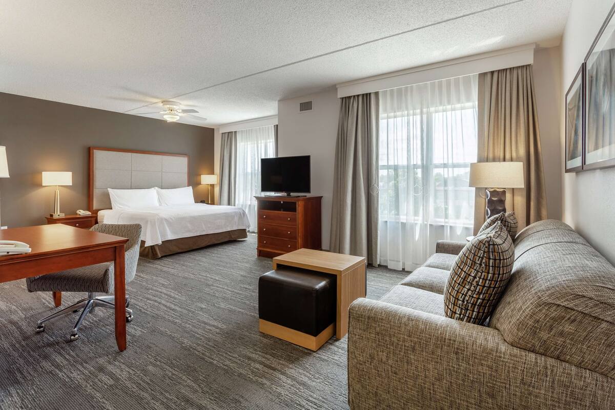 A hotel room with a bed, a desk, a television, a sofa, and a small table.