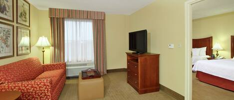 A hotel room with a sofa, a television, a dresser, and a bed.