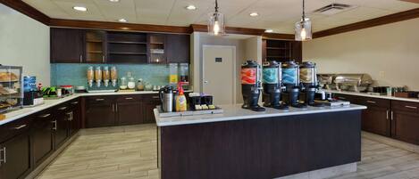 A modern kitchen with dark wood cabinets, a central island with coffee makers, and a tiled backsplash.