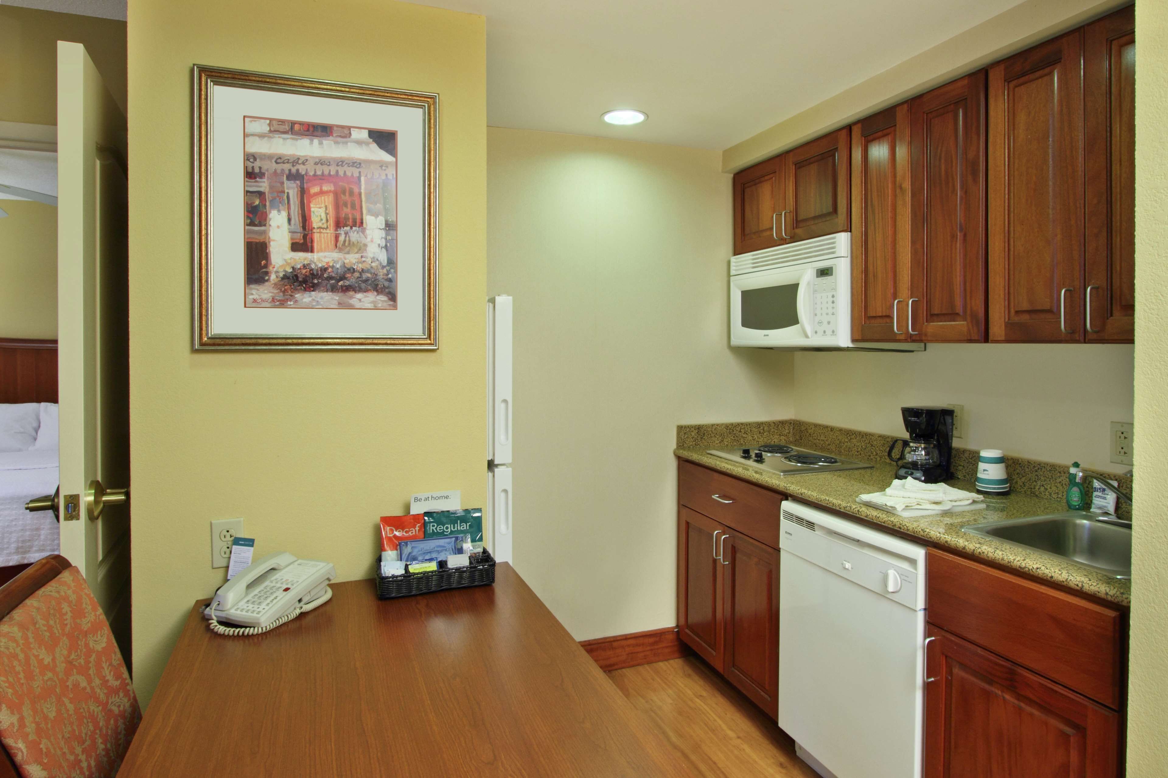 A compact hotel room with a kitchenette, a bed, a telephone, and a framed picture on the wall.