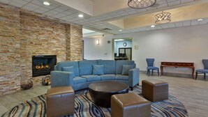 Een moderne woonkamer met een bakstenen muur, een open haard, een blauwe modulaire bank, leren poefs en een kamerbreed tapijt met een patroon.