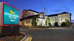 Een hotelentree met een bord voor Homewood Suites Hilton, bestaande uit een groot gebouw met meerdere ramen en een parkeerplaats.