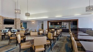 Een restaurantgedeelte in een hotel, met verschillende tafels en stoelen, een bar en een aan de muur bevestigde televisie.
