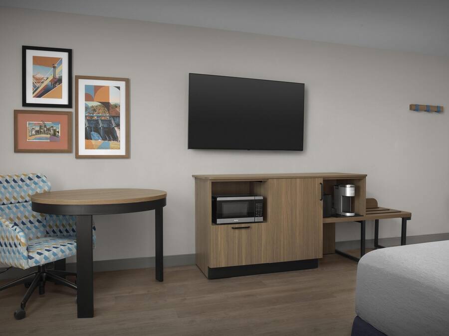 Une chambre d’hôtel avec un lit, un bureau doté d’un micro-ondes, une chaise et des tableaux encadrés au mur.