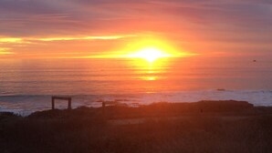 A sunset over the ocean with a bench in the foreground. - Little Sur Inn (Cambria)