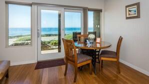 A dining area with a view of the ocean, wooden chairs, a round table, and a bench. - Little Sur Inn (Cambria)