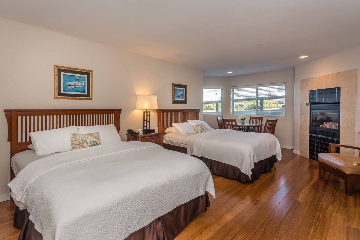 A hotel room with two beds, a wooden headboard, a fireplace, and a dining area with a table and chairs.