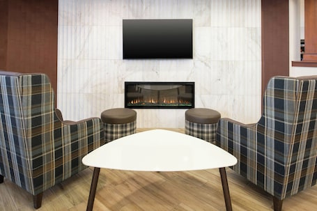 A modern living room with a flat-screen TV mounted above a fireplace, two plaid armchairs, and a white coffee table.. Residence Inn by Marriott Columbia