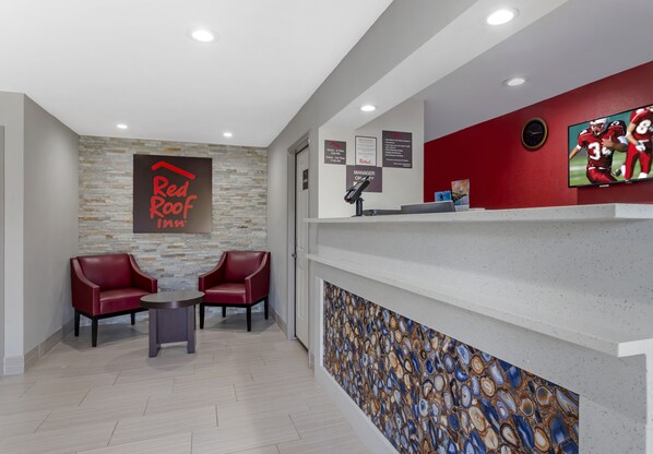 Un área de recepción con el letrero de Red Roof Inn, un mostrador de recepción, un televisor y dos sillones de cuero rojo.