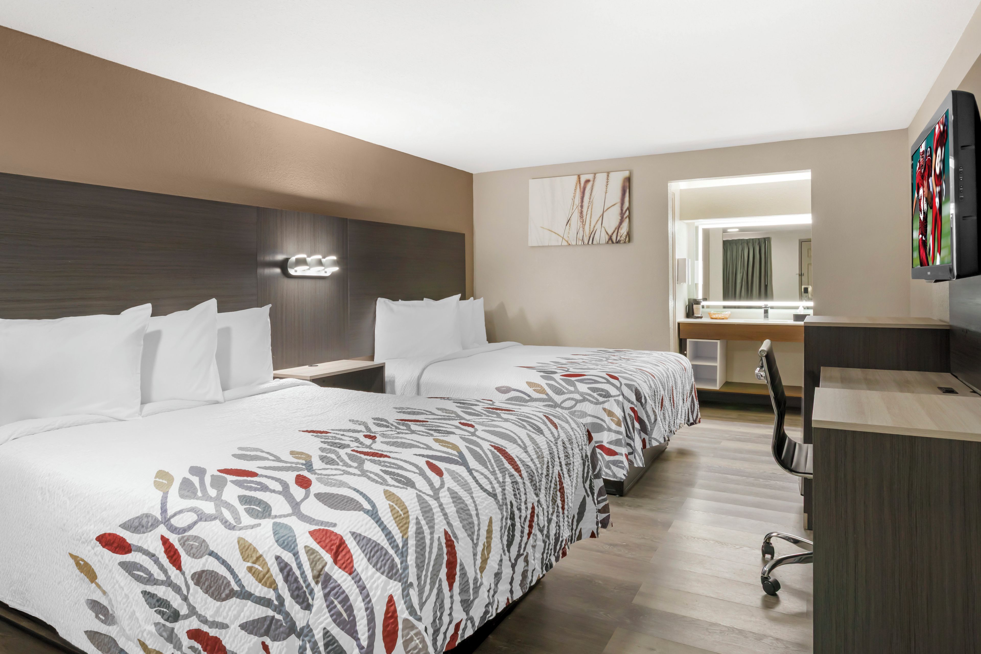 A hotel room with a large bed, a desk, a mirror, and a television.