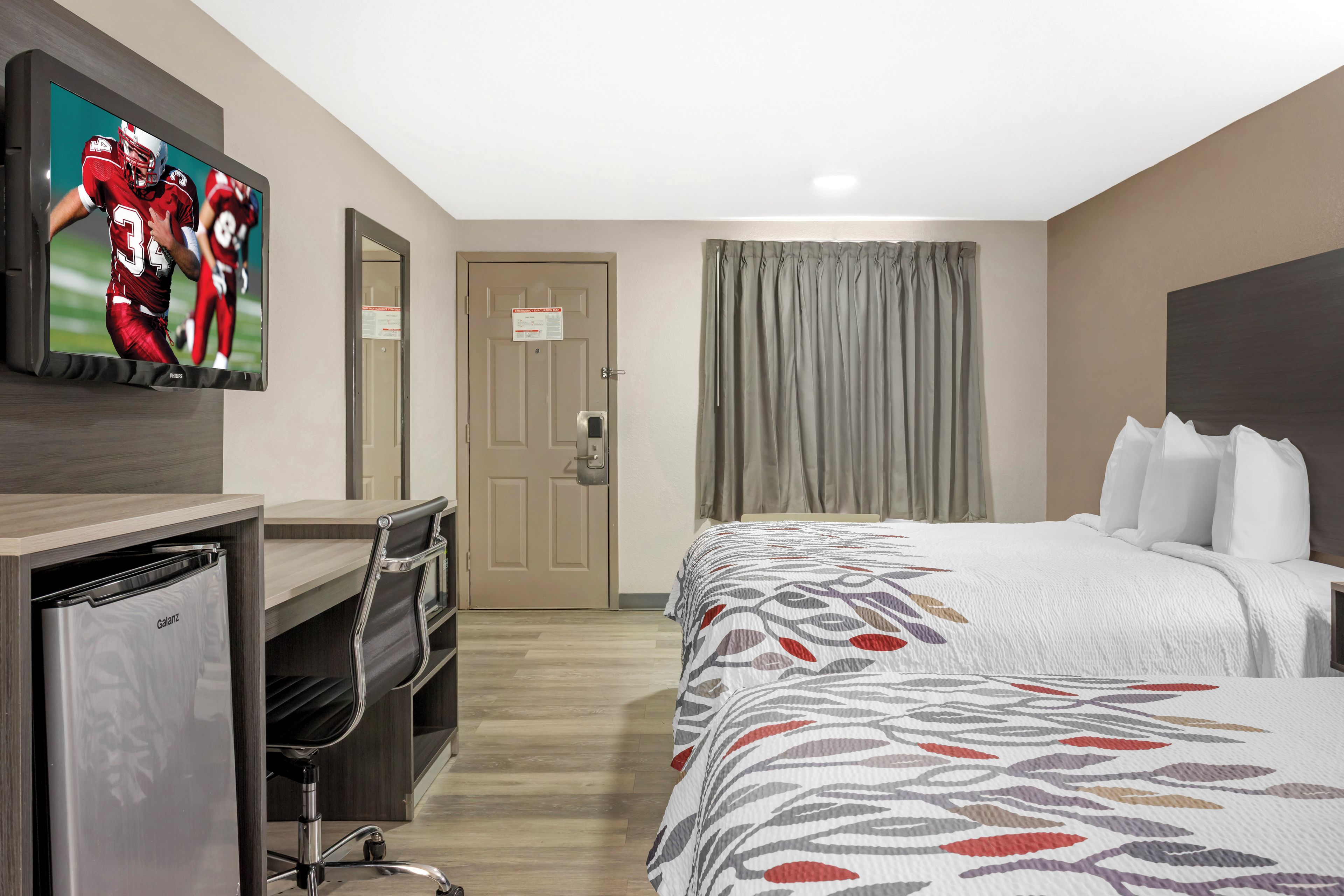 A hotel room with a bed, a desk, a television, and a door.