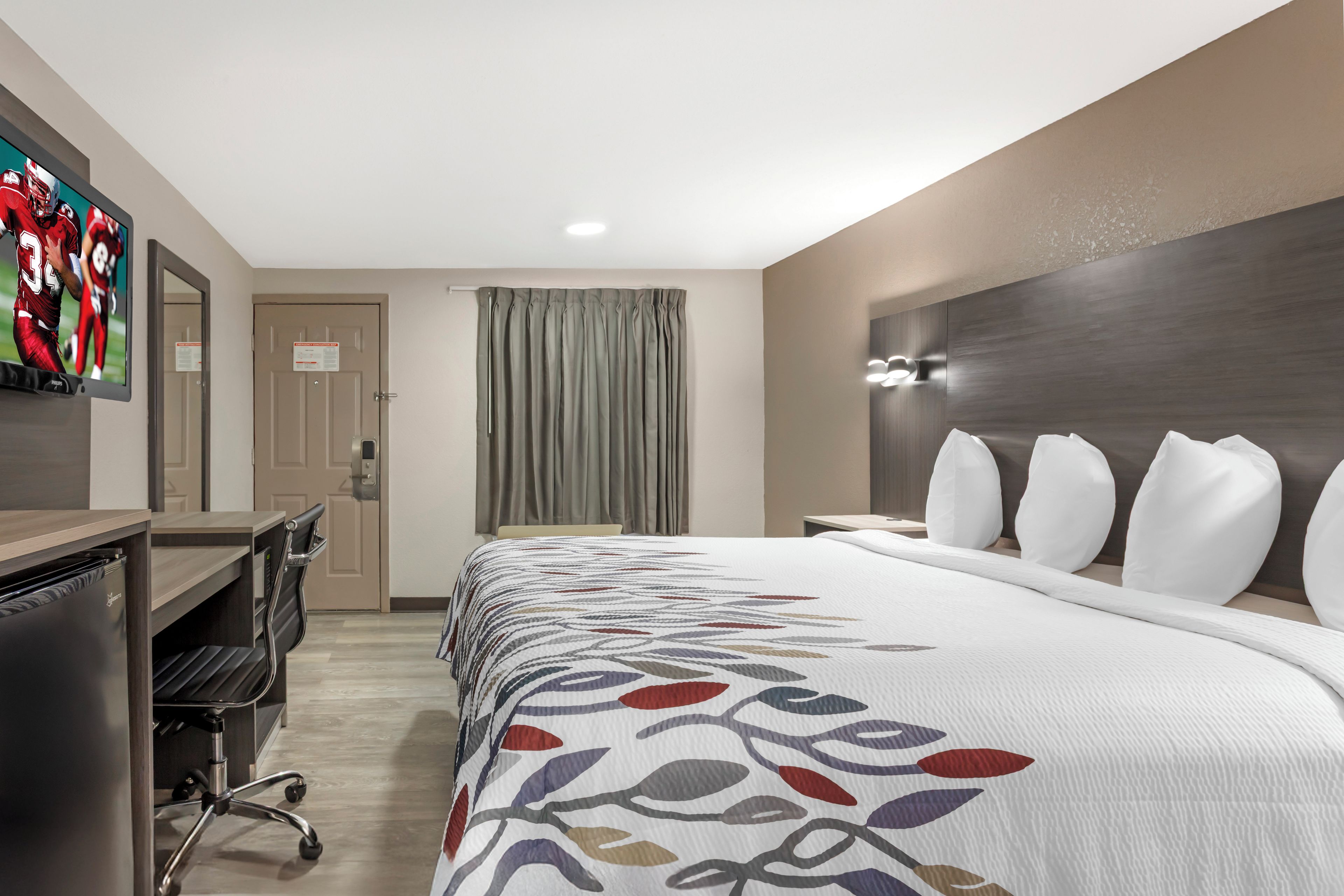 A hotel room with a bed, a desk, a chair, a television, and a door.