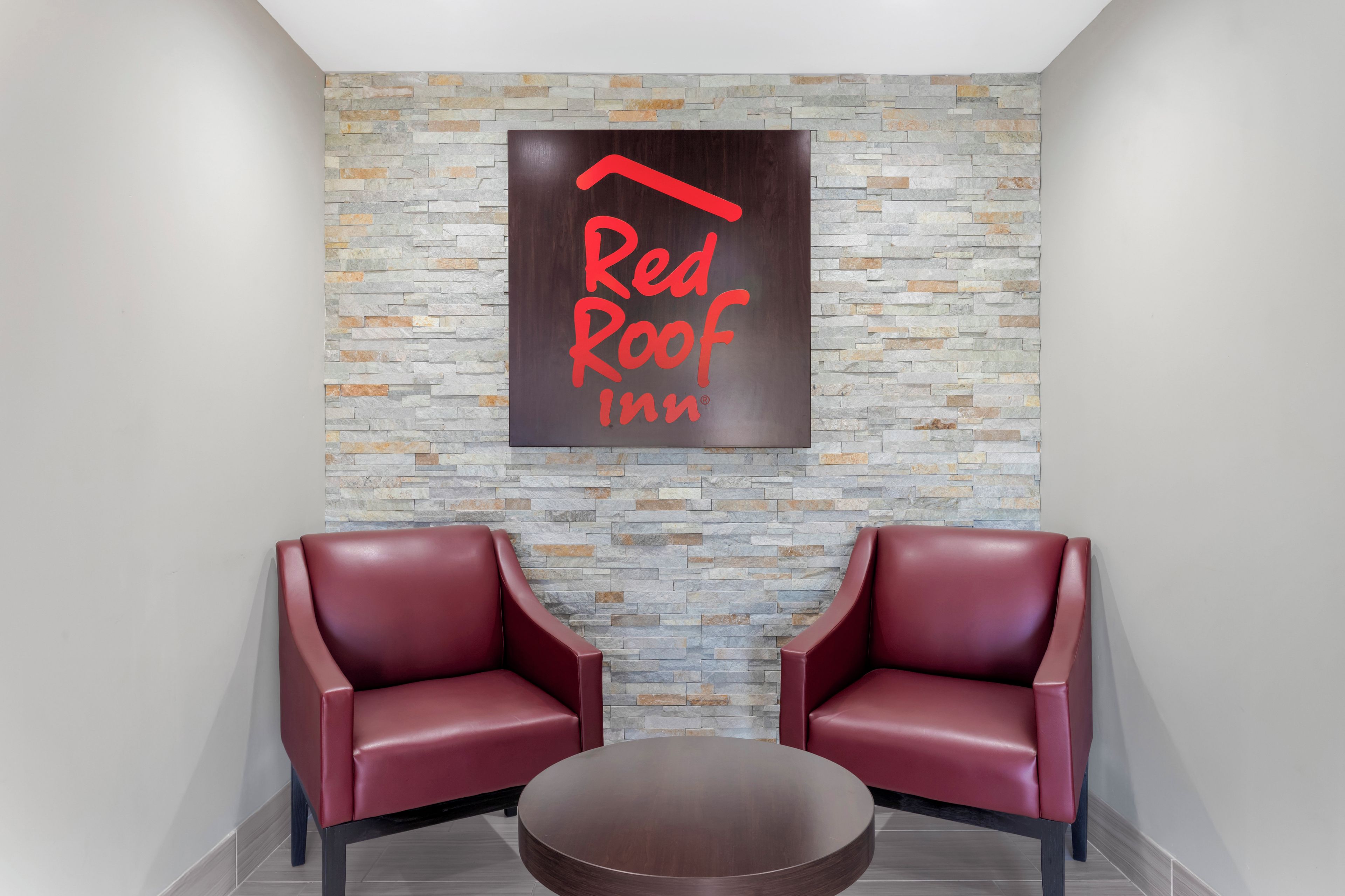 Une enseigne Red Roof Inn, avec deux fauteuils en cuir rouge et une table ronde dans un espace d’accueil.