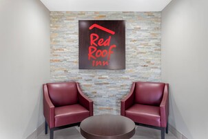 Señal de Red Roof Inn con dos sillones de cuero rojo y una mesa redonda en un área de recepción.