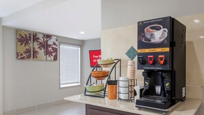 Une machine à café proposant différentes options : café normal, eau chaude et café décaféiné, ainsi qu’un bol de fruits posé sur le comptoir.