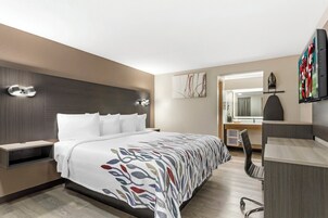 Quarto de hotel moderno com uma cama grande, uma escrivaninha, uma cadeira e uma televisão.
