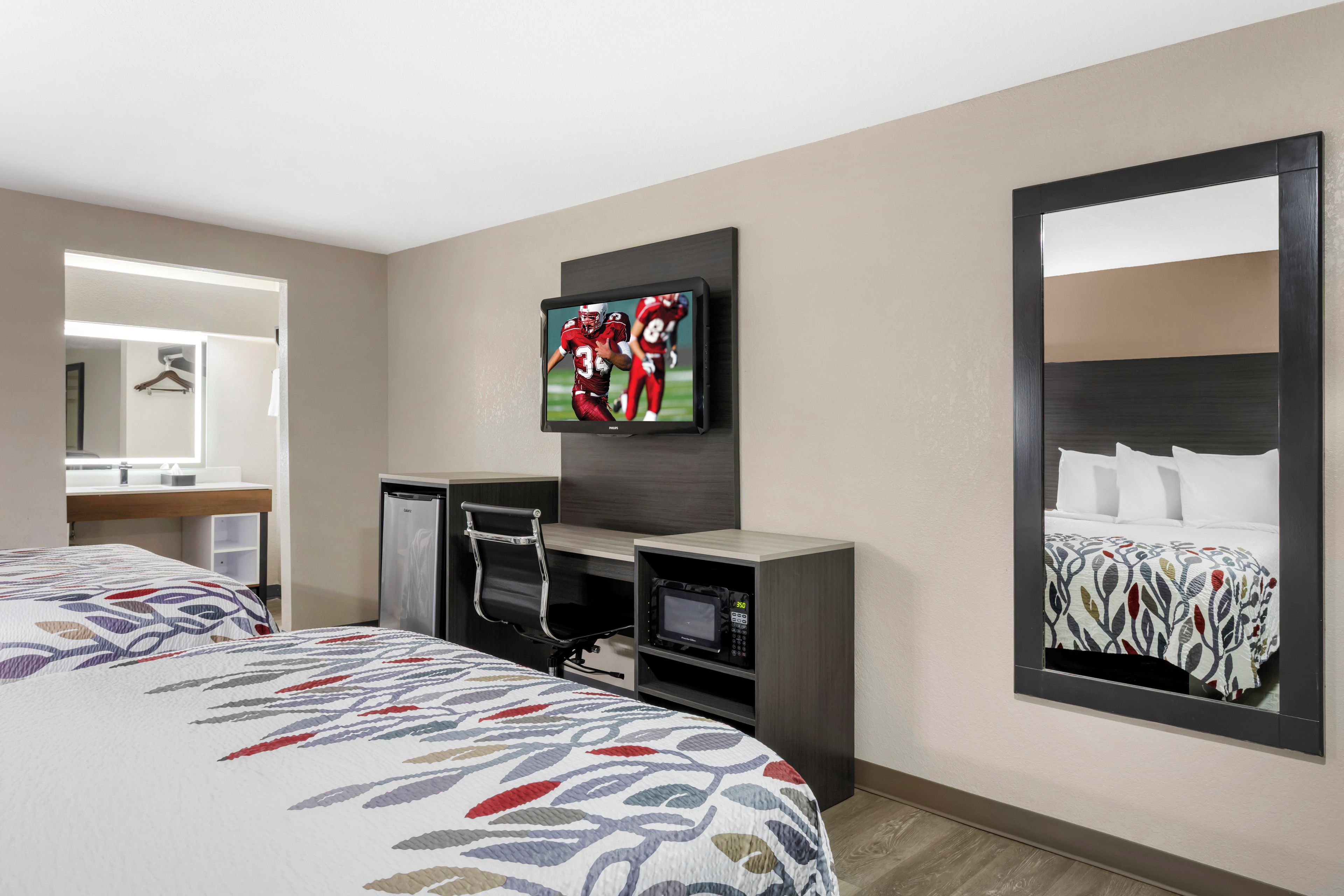 A hotel room with a bed, a desk with a computer, a television, a mirror, and a microwave.