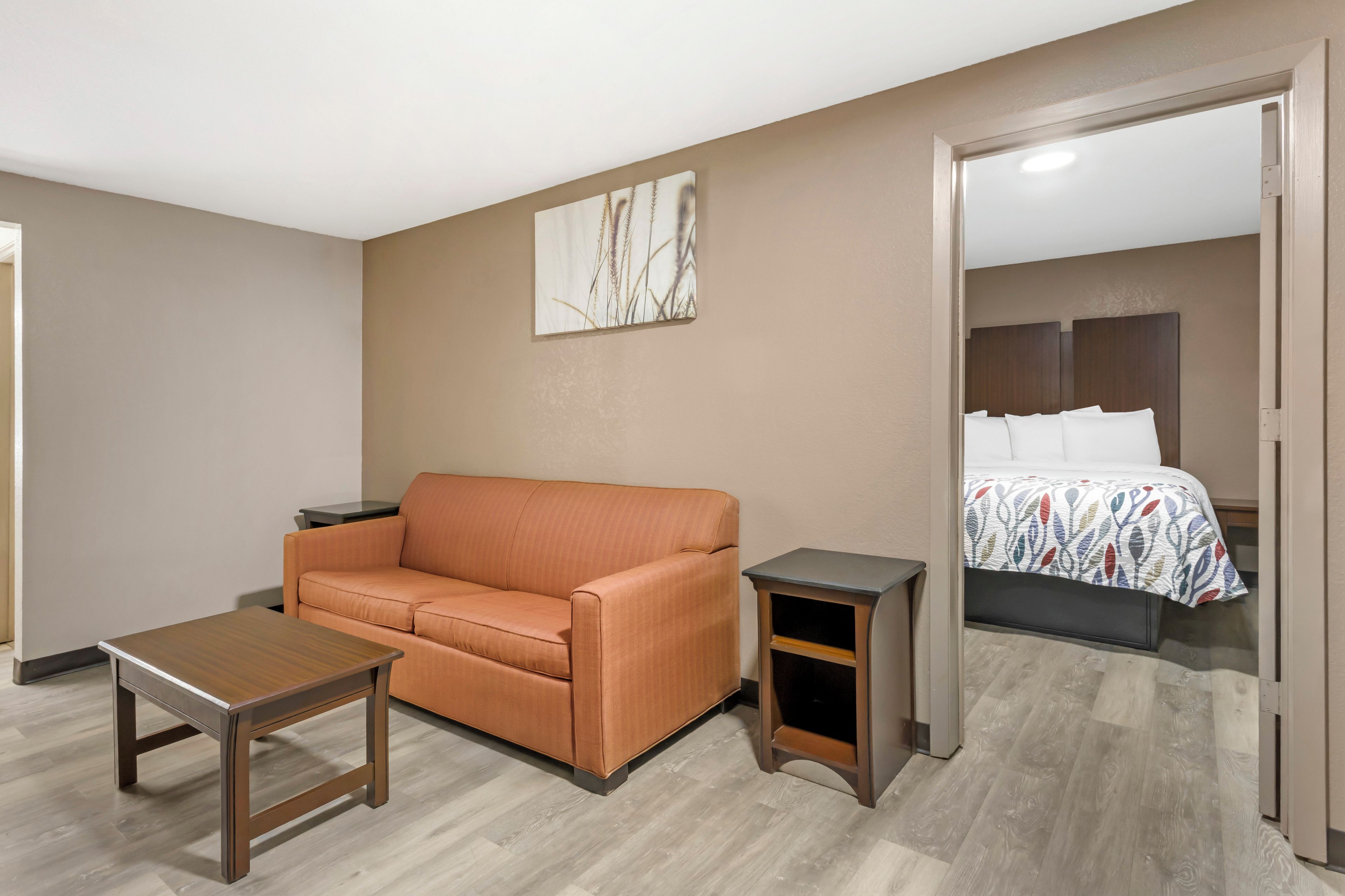 Habitación de hotel con sofá, una mesita, una lámpara de noche y una cama con colcha estampada.