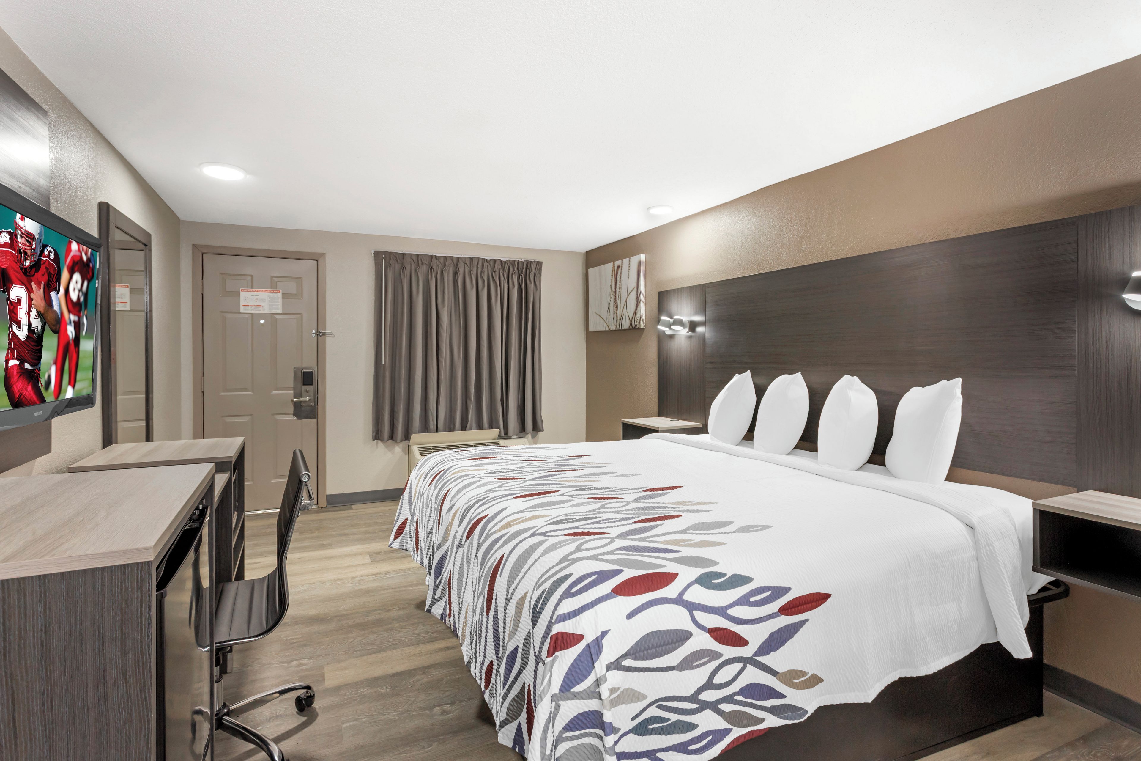 Une chambre d’hôtel équipée d’un lit, d’un bureau, d’une chaise, d’une télévision et d’un luminaire fixé au mur.
