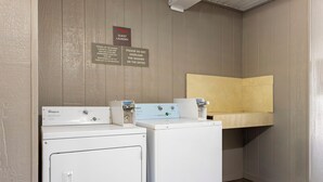 Un espace buanderie équipé de deux lave-linge Whirlpool, d’un panneau indiquant qu’il s’agit de la buanderie réservée aux clients, et d’un avertissement concernant le risque de surcharge des machines.