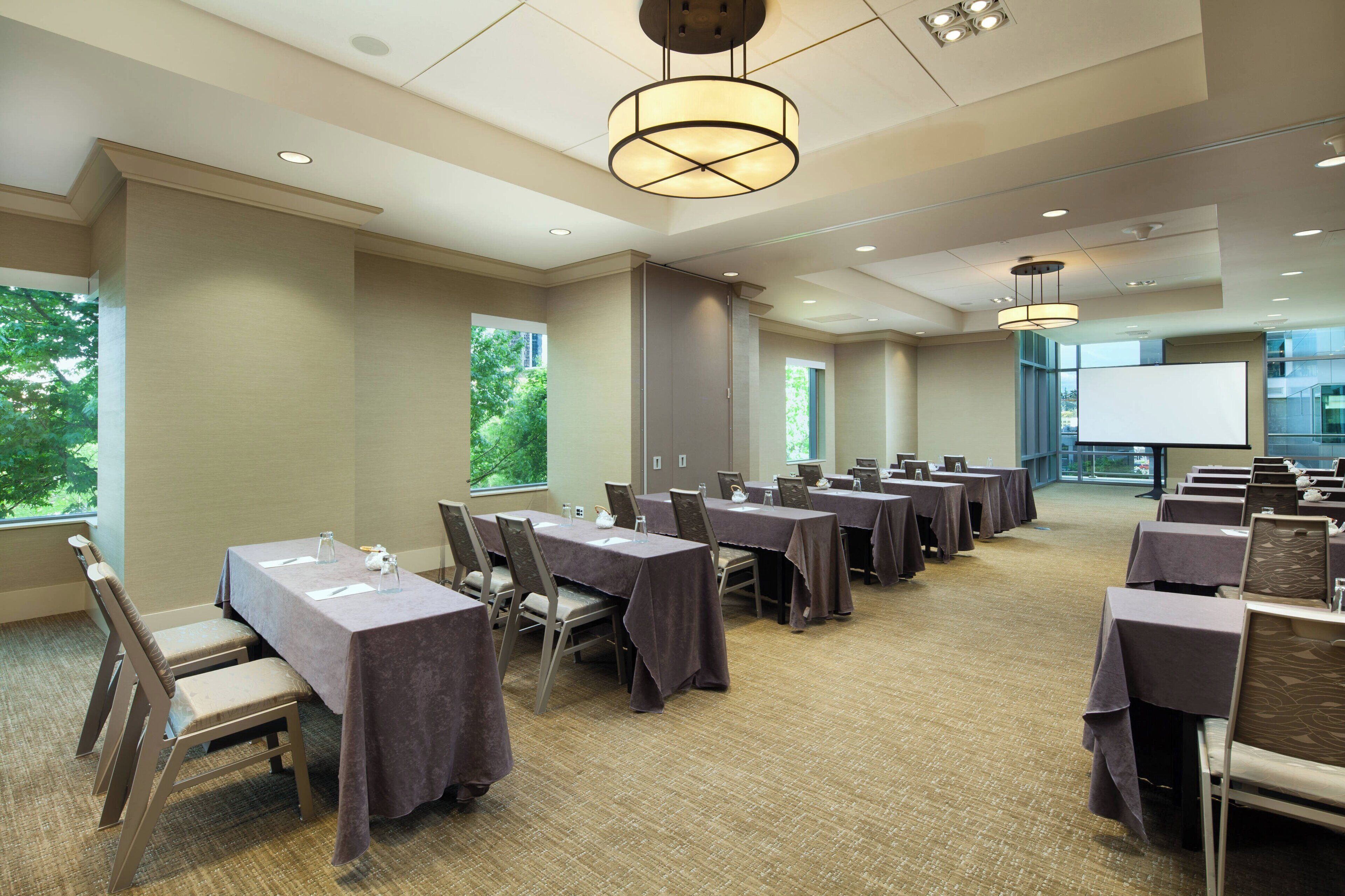 A conference room with multiple tables, chairs, and a projector screen.