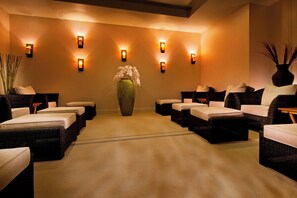 A spa room with multiple massage tables arranged in a row, a large vase with flowers, and wall-mounted lighting. - The Westin Bellevue (Bellevue)