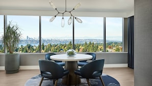 A modern dining area with a round table, two chairs, a potted plant, and a view of a cityscape through large windows. - The Westin Bellevue (Bellevue)