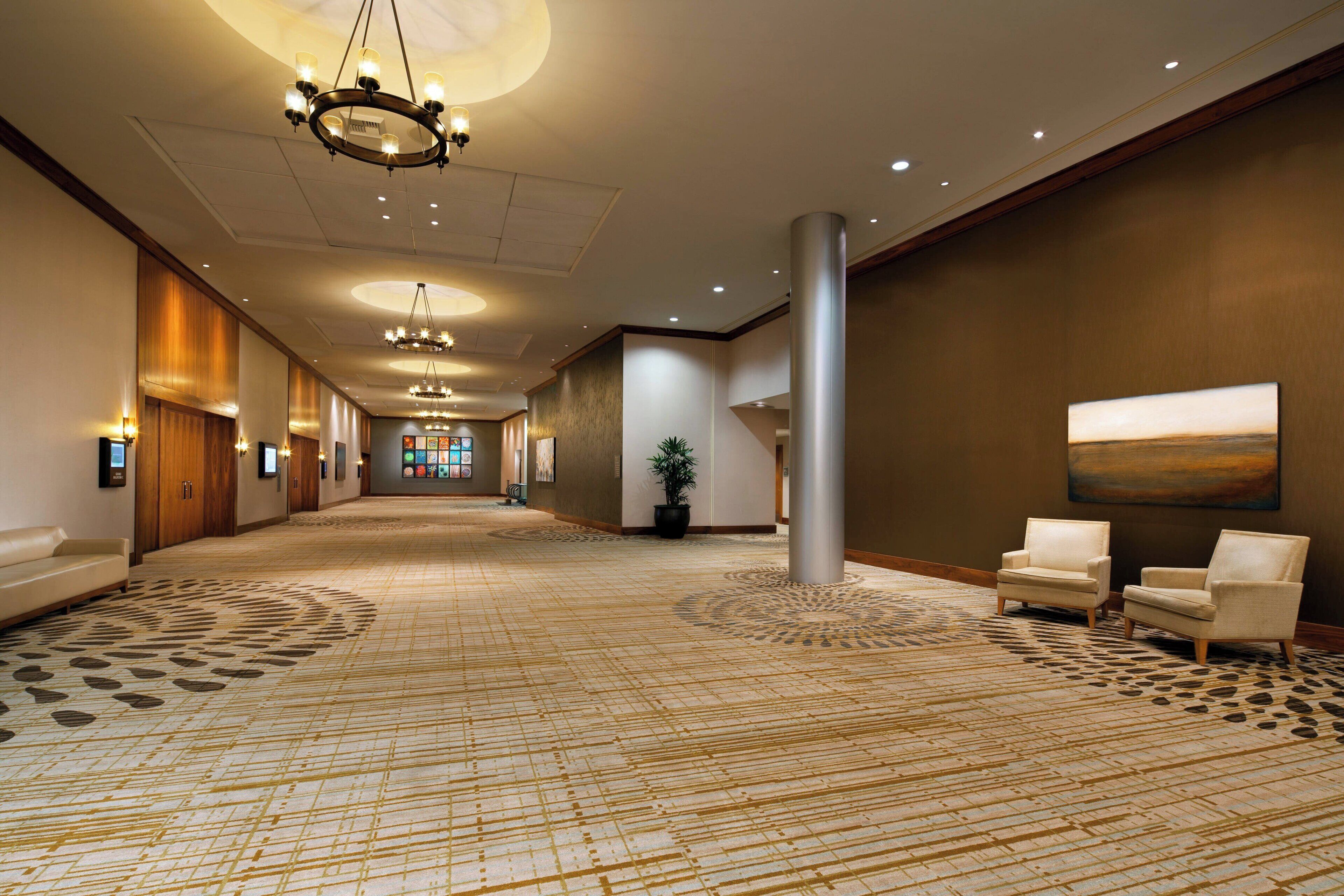 Un hall d’hôtel spacieux, agrémenté d’un tapis à motifs, d’un lustre et d’un grand tableau mural.