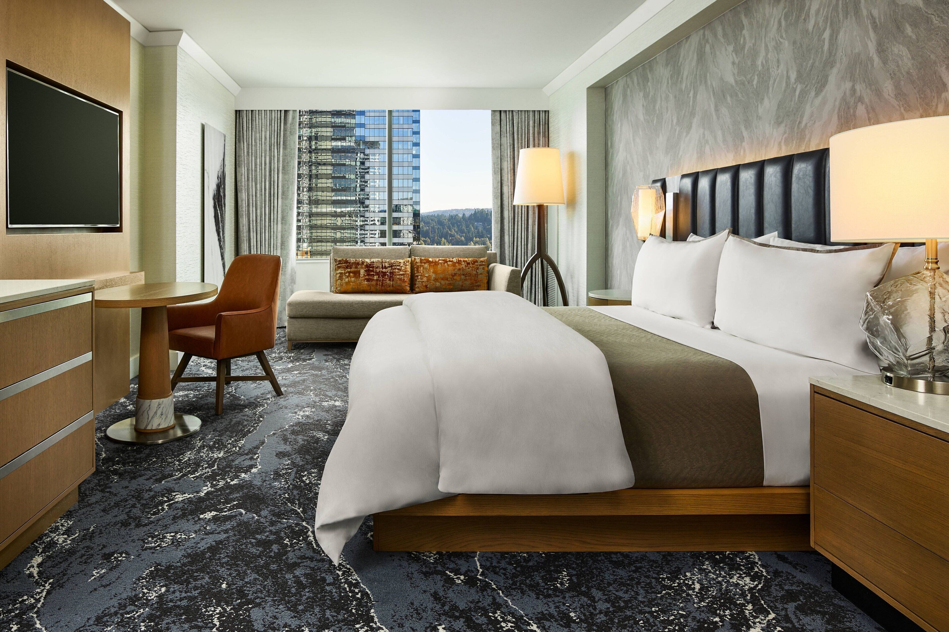 Une chambre d’hôtel avec un grand lit, un bureau, une chaise et une vue sur le paysage urbain.