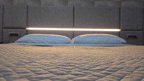 Un lit avec une couverture matelassée, deux oreillers et une tête de lit dotée d’une bande lumineuse.