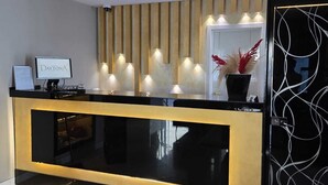 Un comptoir d’accueil avec un écran d’ordinateur, une plante en pot et un mur orné d’appliques murales verticales.